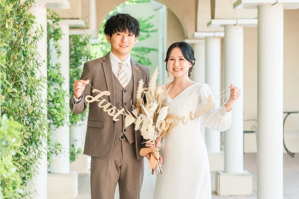 「Just Married」のガーランドとブーケを持って微笑むウェディング姿の男女